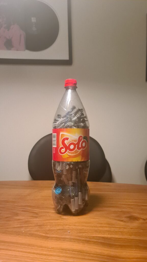 A solitary soda bottle on a table, containing spent needles, with caps covering the needle point